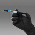 Kuraray Clearfil AP-X Esthetic Flow dental material in a syringe held by a gloved hand for precise application